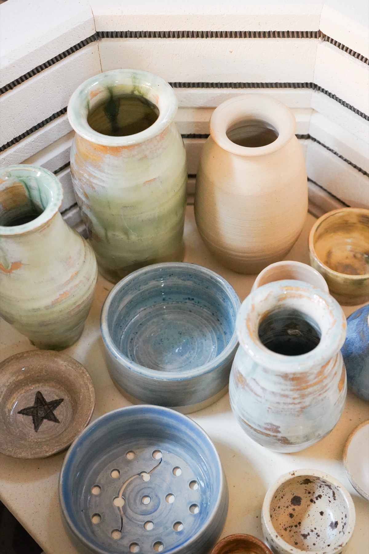 Glazed jars, a star-stamped dish, and a blue colander on the kiln shelf