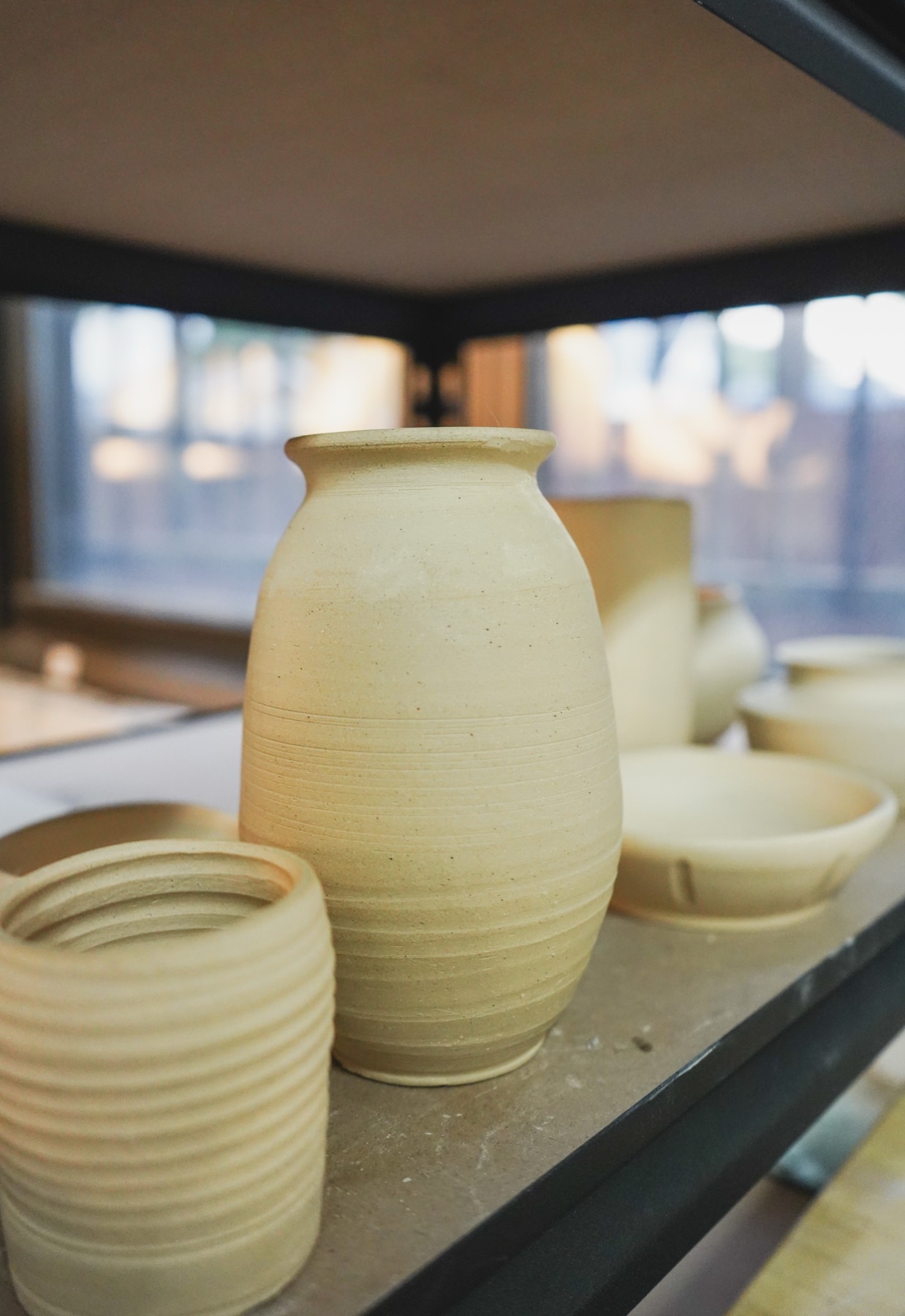 An unglazed vase and pots on the shelf by the window