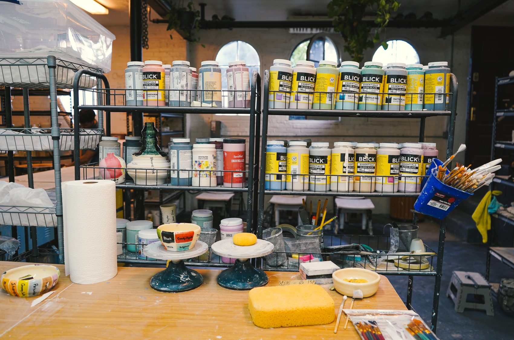 A glazing table scattered with brushes, sponges, and jars of colored glaze