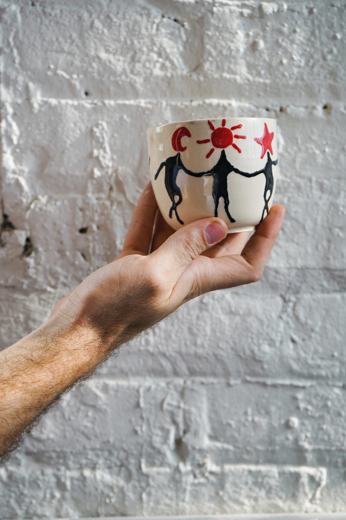 A member's hand-painted mug with a sun and two dancing figures, held up to the light