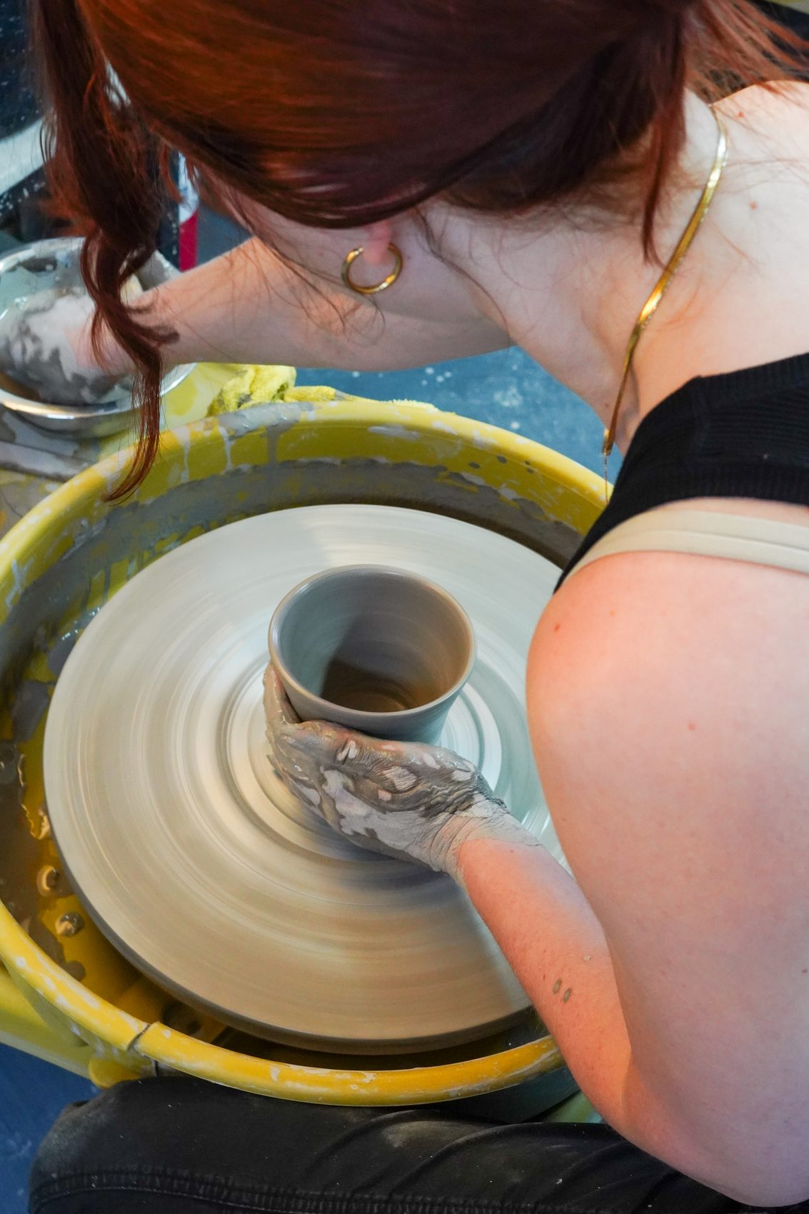 An overhead view of a member centering a cylinder on the wheel, hands wet with clay