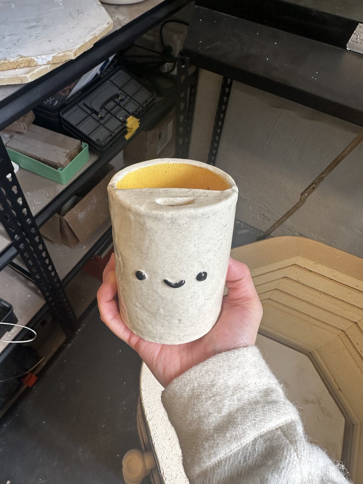 A member holding a hand-thrown mug with a simple smiling face painted on it