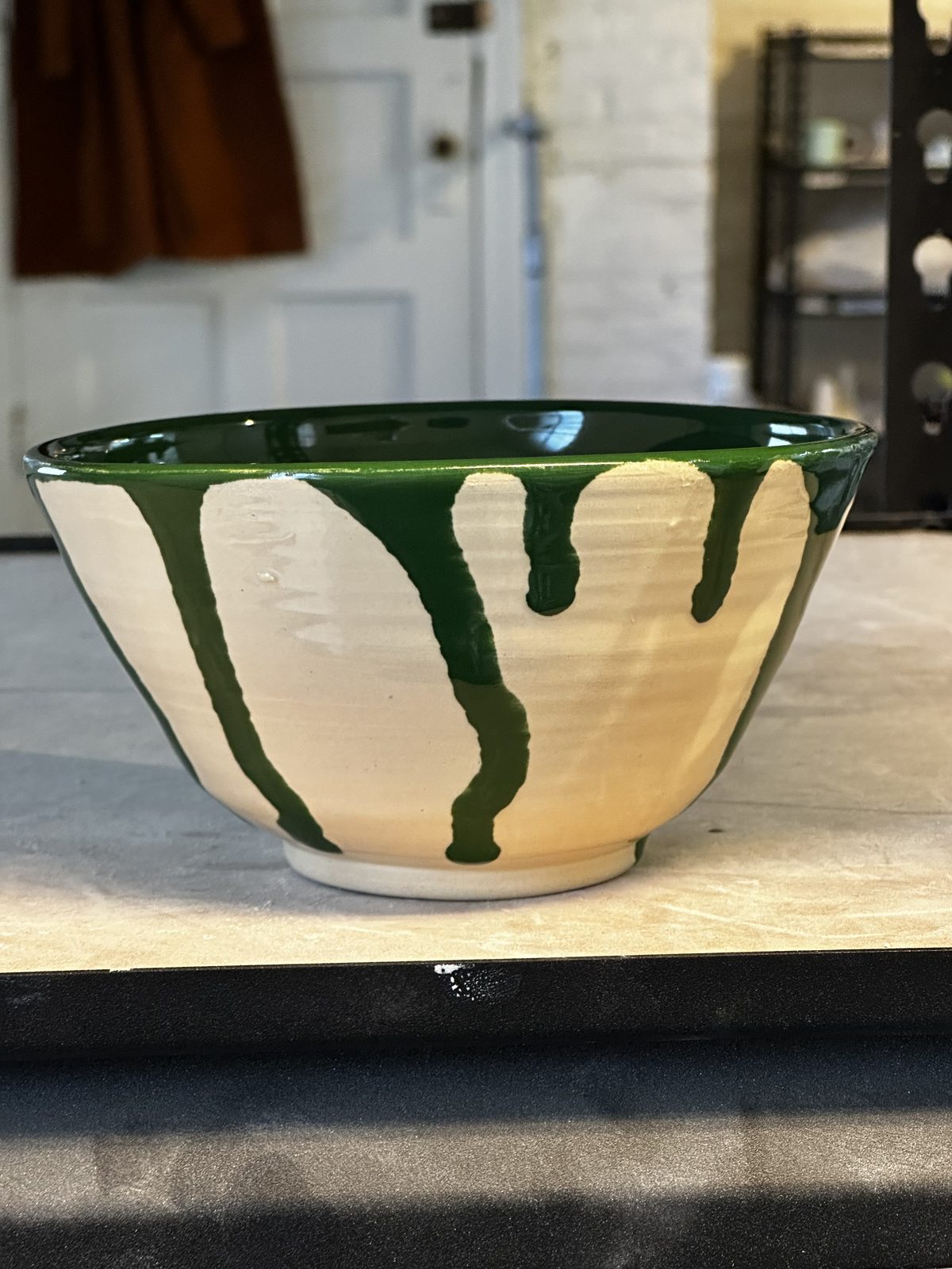 A bowl with a green drip glaze over cream stoneware