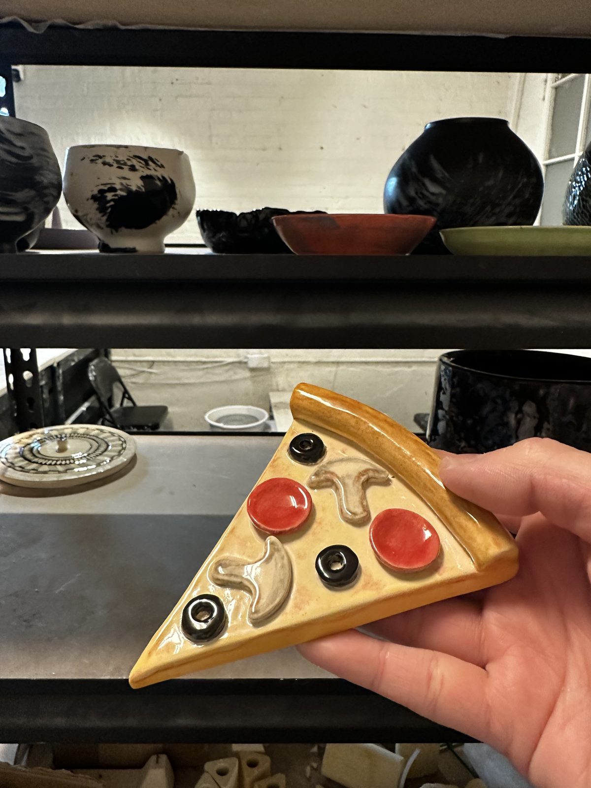 A member holding a ceramic piece sculpted and glazed to look like a pizza slice