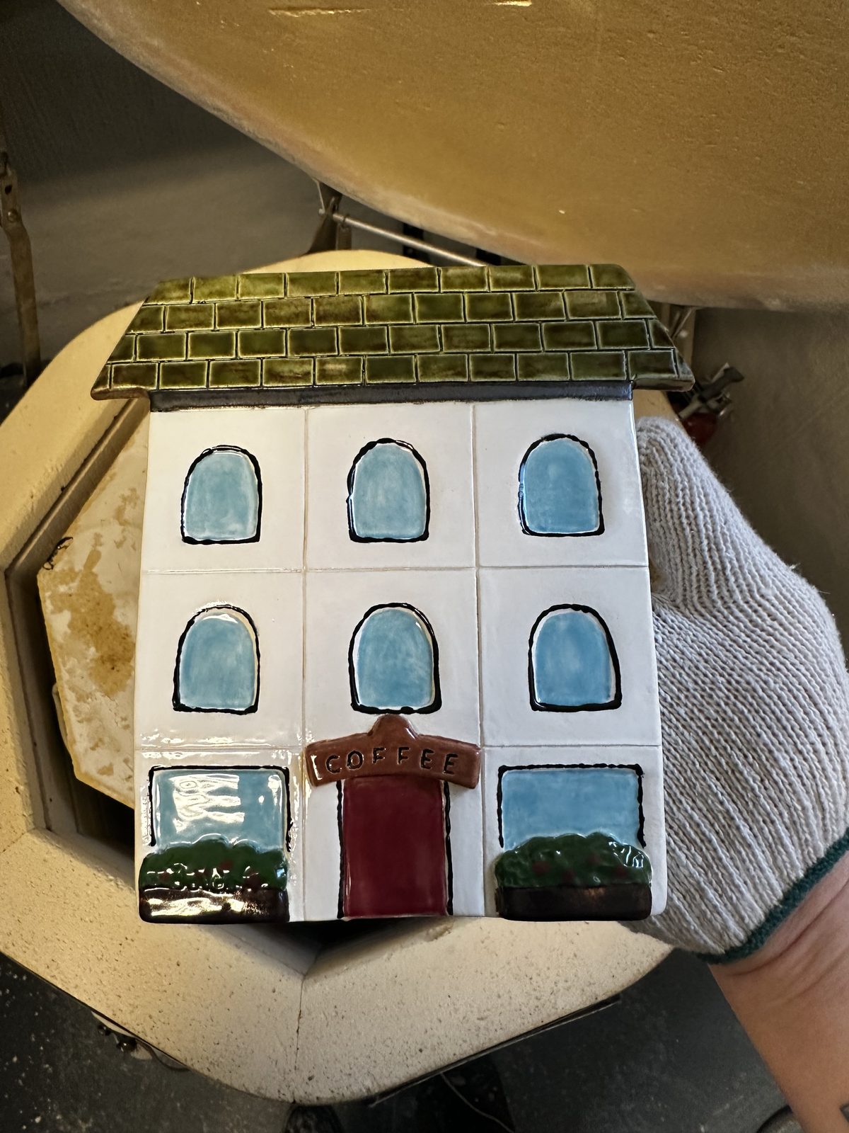 A ceramic house-shaped sculpture with painted blue windows