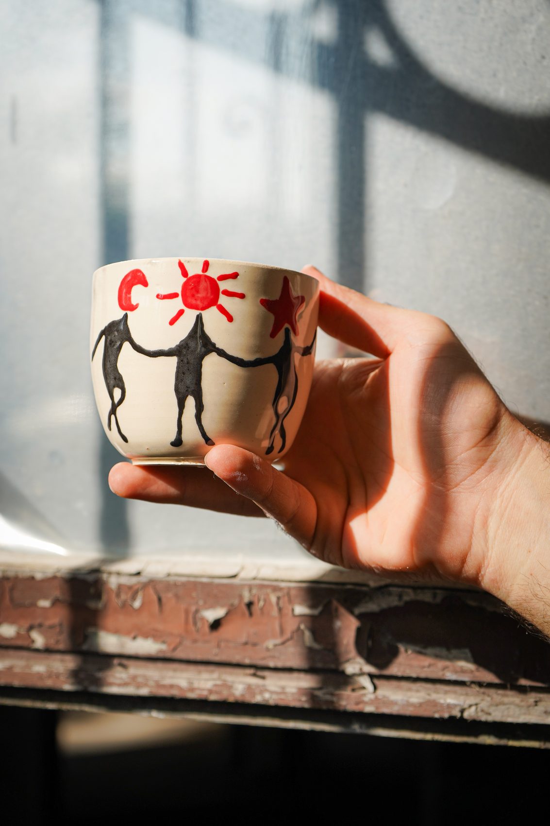 A member's hand holding a hand-painted mug with a sun, moon, and star design