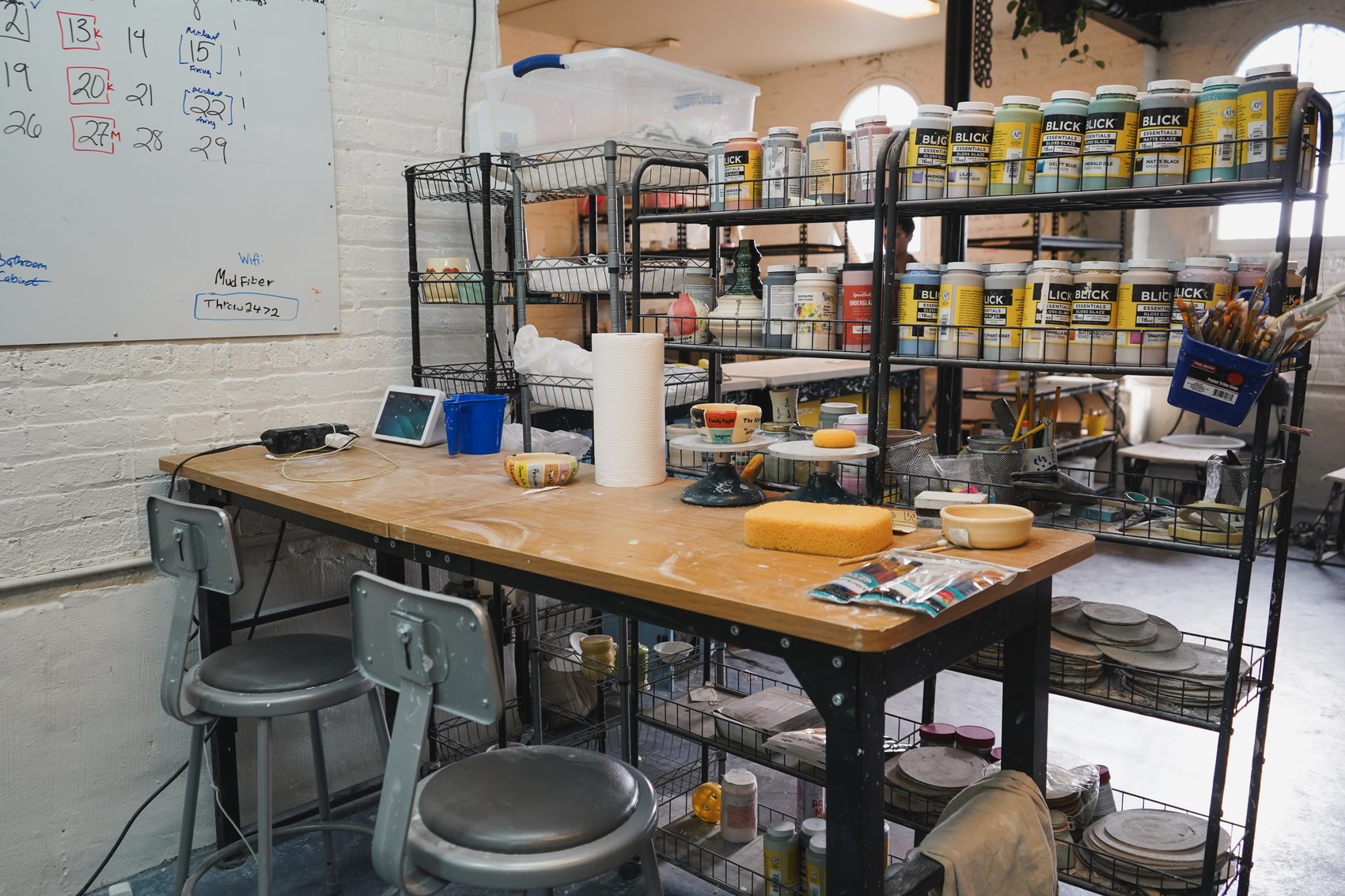 A glazing worktable with brushes and tools, shelves of glaze behind it